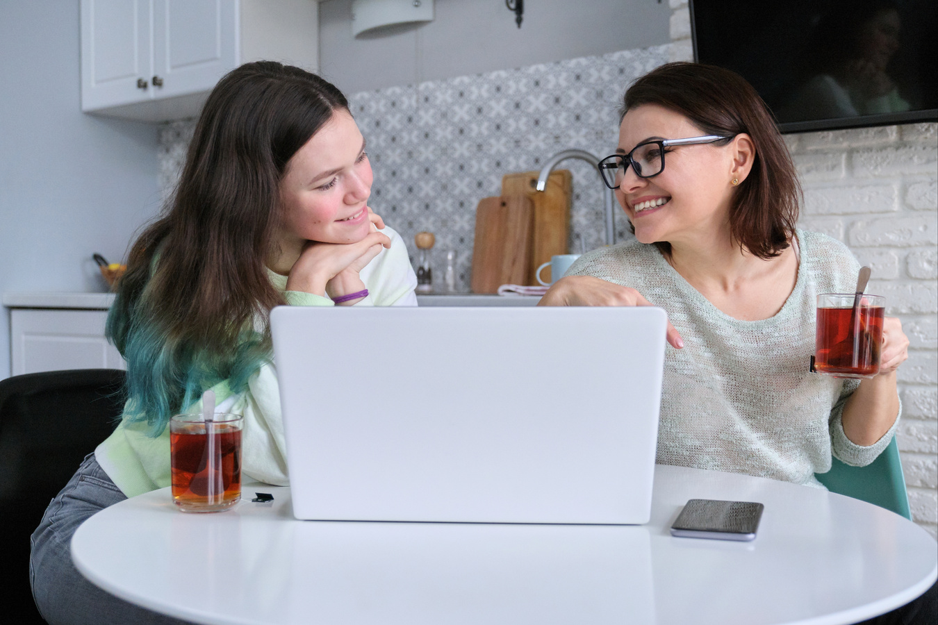 Parent and Teenager Sitting at Home in Kitchen and Looking at Laptop Screen